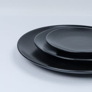 Matte black ceramic dinner plates stacked in graduated sizes on white background.