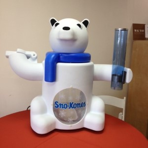 White and blue bear-shaped robotic Sno-Kone machine sitting on red surface.