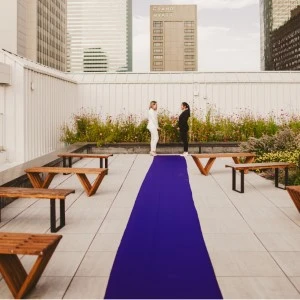 Purple runner highlights rooftop event space with wooden picnic tables and urban backdrop.