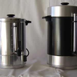 Two metallic silver coffee urns with black lids, side by side on a white surface.